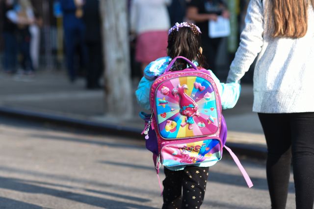 a child with a colorful pink troll backpack is walking towards school
